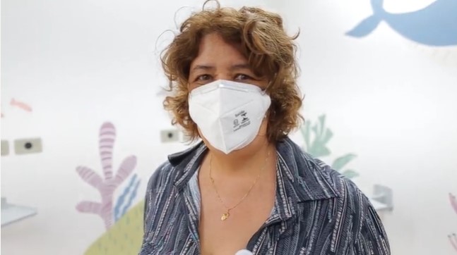 Solange está tem os cabelos curtos e está olhando para a foto. Ela usa uma camisa azul com listras.